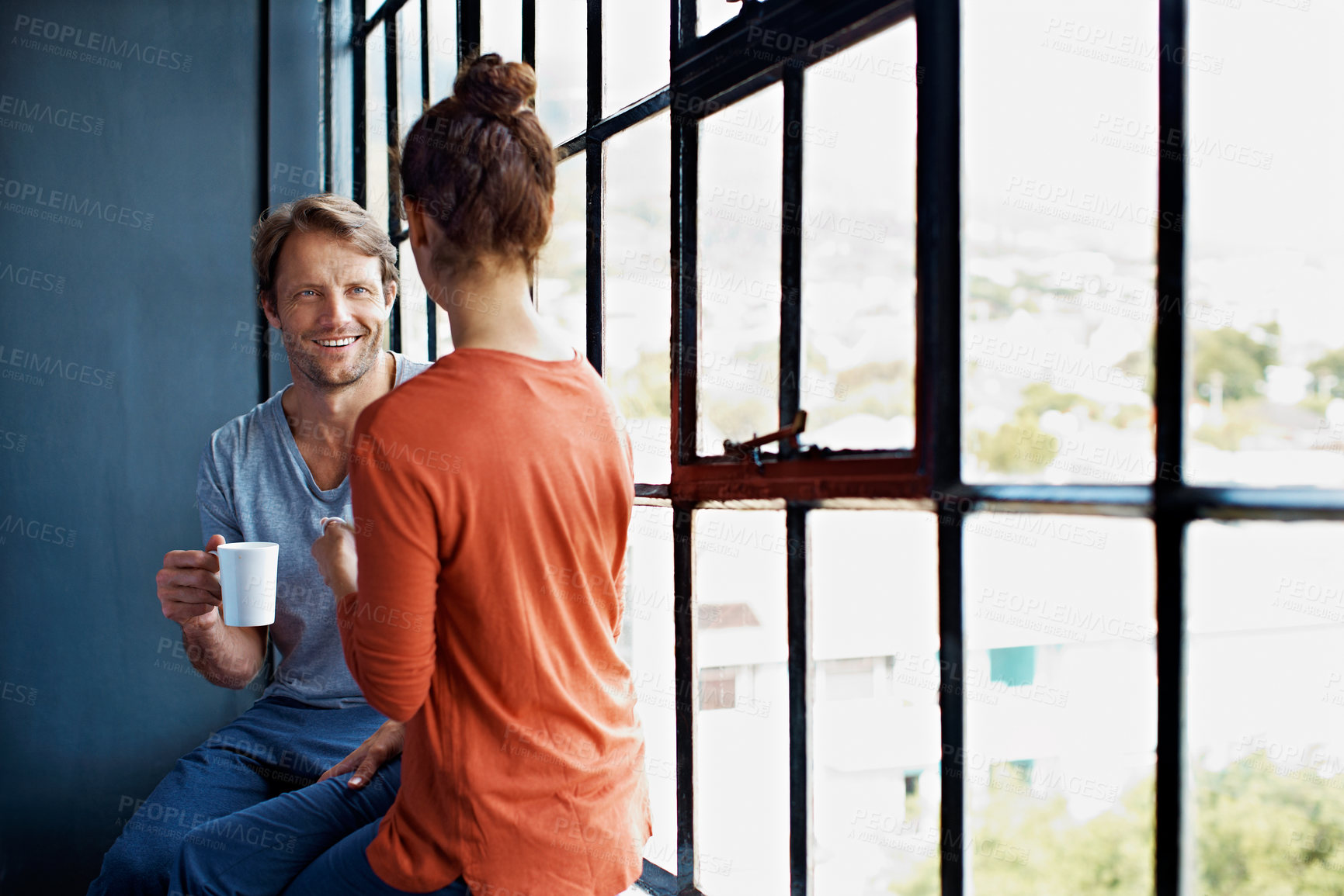 Buy stock photo Shot of a happy mature couple sitting on a window sill at home drinking coffee and talking together