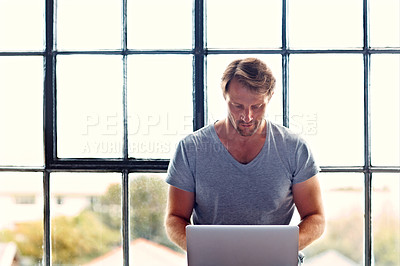 Buy stock photo Shot of a mature man sitting on a window sill at home using a laptop