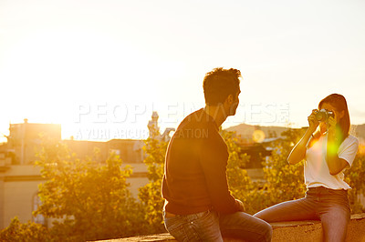 Buy stock photo Shot of a young woman taking a photo of her boyfriend while sitting on a balcony overlooking the city
