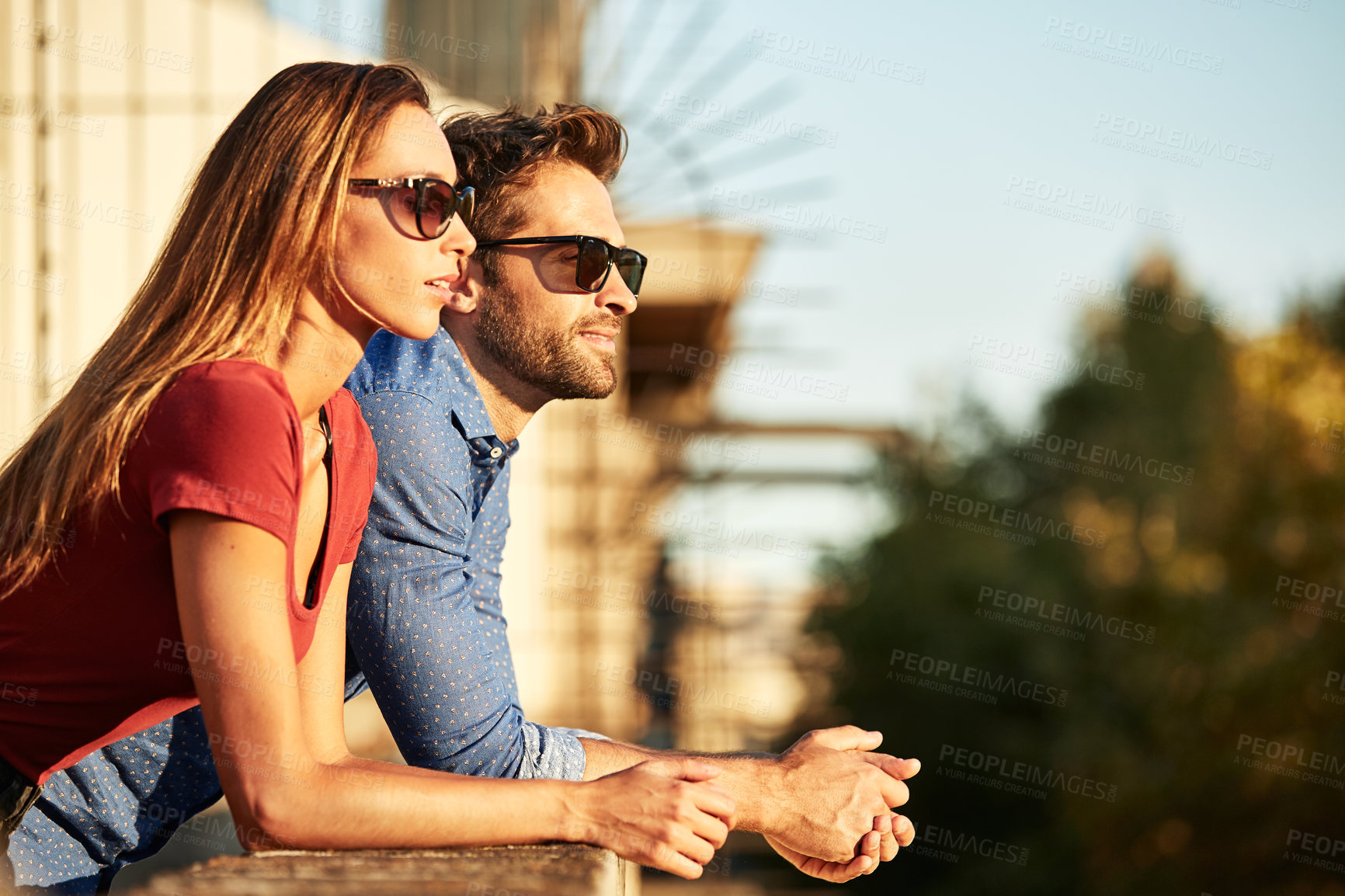 Buy stock photo Shot of a smiling young couple leaning on a balcony in the city looking at the view