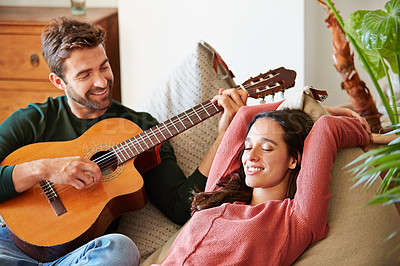 Buy stock photo Shot of a young man playing guitar for his girlfriend while relaxing in their living room