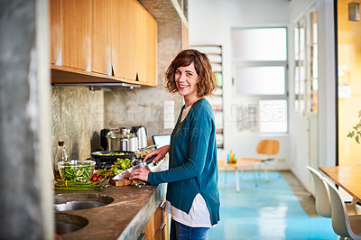 Buy stock photo Portrait of a smiling young woman preparing a meal in her kitchen