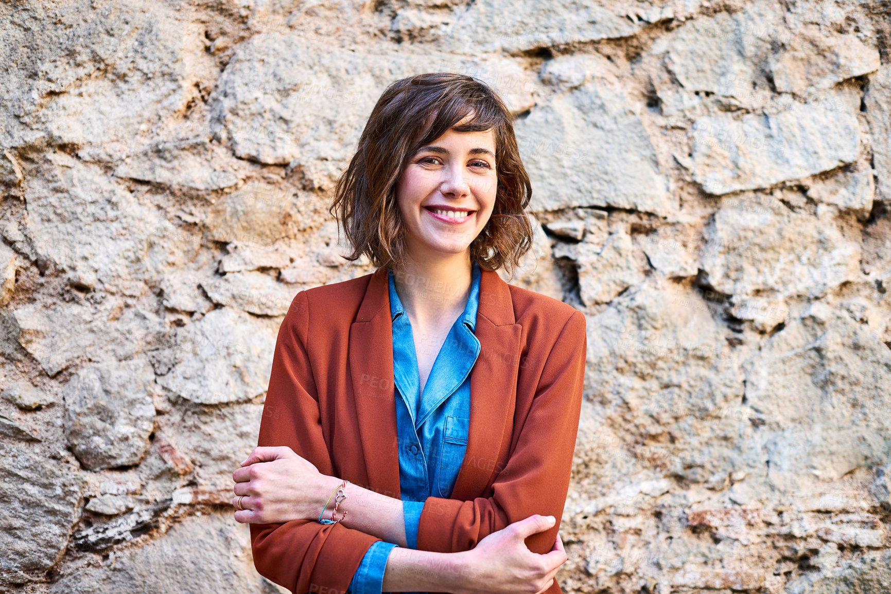 Buy stock photo Portrait of a smiling young woman standing outside in front of a stone wall