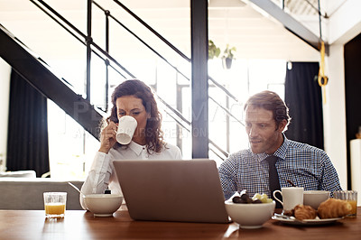 Buy stock photo Shot of a professional couple sitting at the dining table eating breakfast and using a laptop