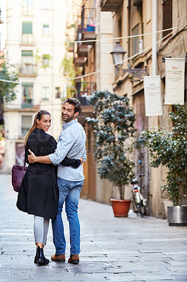 Buy stock photo Rearview shot of an affectionate young couple walking arm in arm together in the city