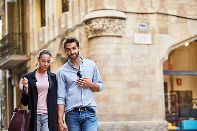 Buy stock photo Shot of an affectionate young couple walking hand in hand together in the city