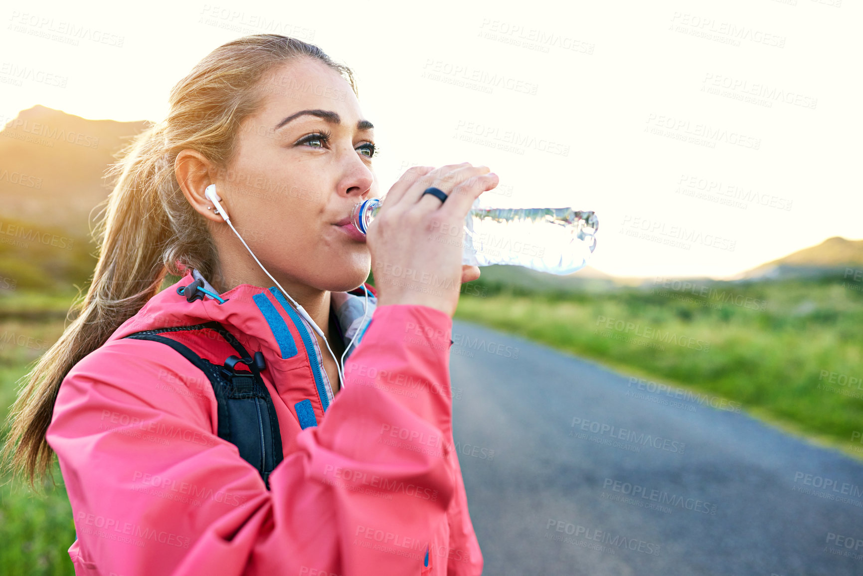 Buy stock photo Shot of a young woman drinking from a water bottle while taking a break from an early morning run