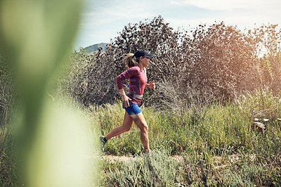 Buy stock photo Shot of a focused young woman running alone on a trail outdoors
