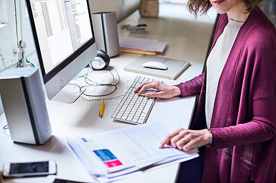 Buy stock photo Shot of a young woman sitting at a desk in her home office reading documents and working on a computer