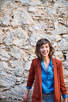Buy stock photo Portrait of a smiling young woman standing outside in front of a stone wall