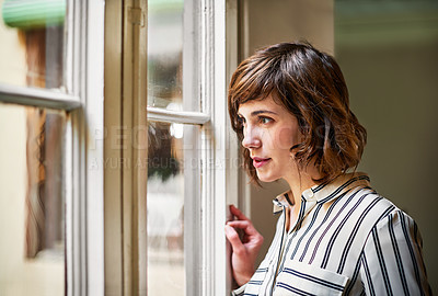 Buy stock photo Shot of a young woman looking out through a window at home