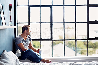 Buy stock photo Shot of a mature man sitting on a window sill at home drinking a cup of coffee