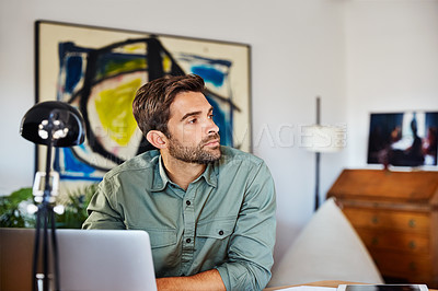 Buy stock photo Shot of a young man sitting at a table at home working on a laptop