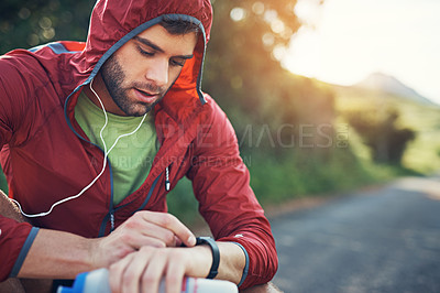 Buy stock photo Shot of a young man drinking water and checking his watch while out for a run