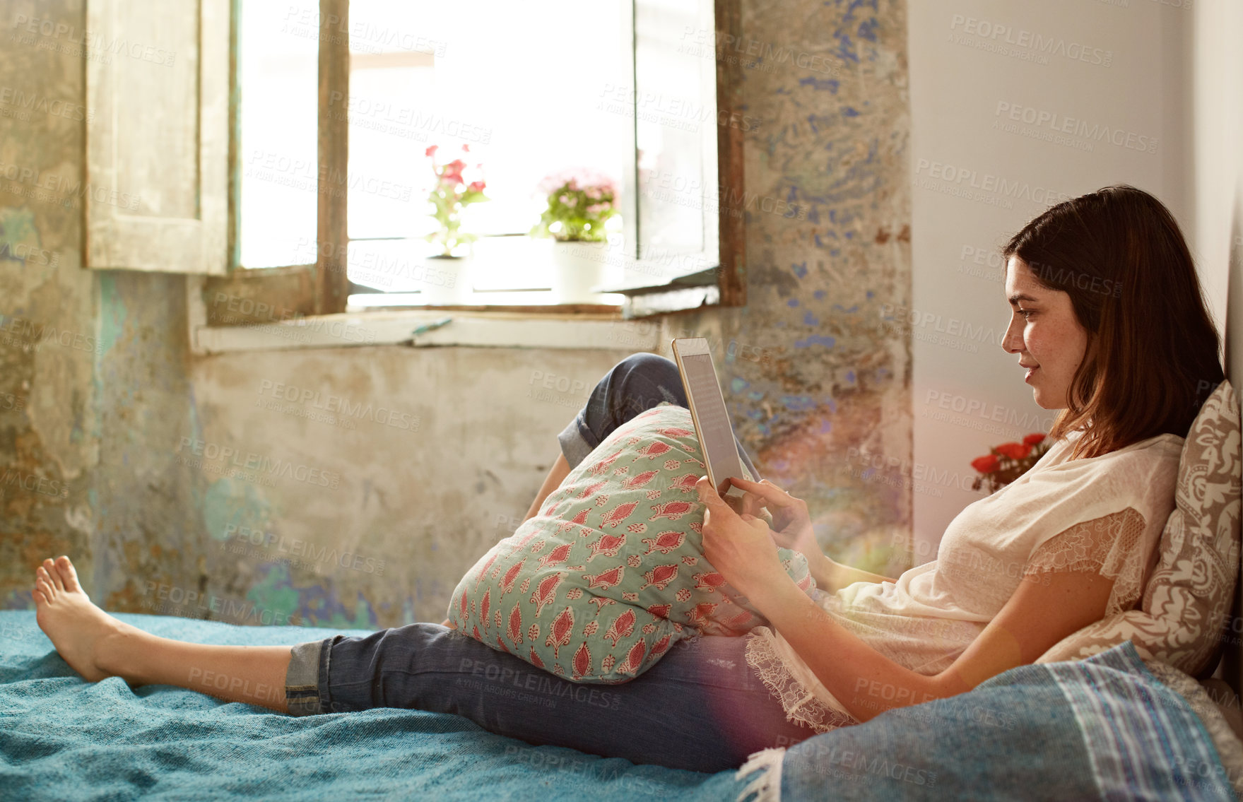 Buy stock photo Shot of a young woman lying on her bed using a tablet