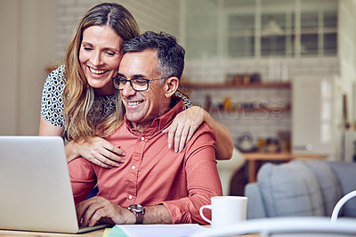 Buy stock photo Shot of a mature woman leaning on her husband while he works on his laptop