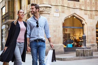 Buy stock photo Shot of an affectionate young couple walking hand in hand together in the city