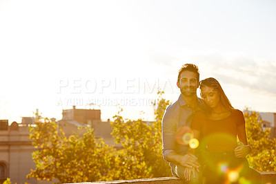 Buy stock photo Shot of a affectionate young couple sitting on a rooftop together at sunset