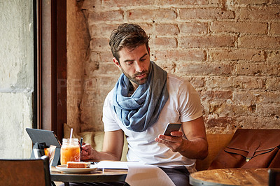 Buy stock photo Shot of a handsome young man using his cellphone while sitting in a cafe
