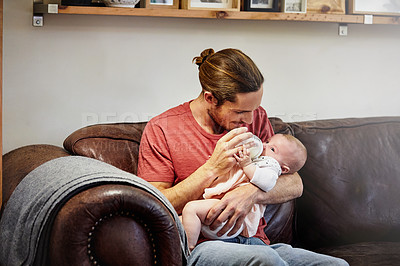 Buy stock photo Shot of a handsome young man feeding his newborn baby girl on the sofa at home