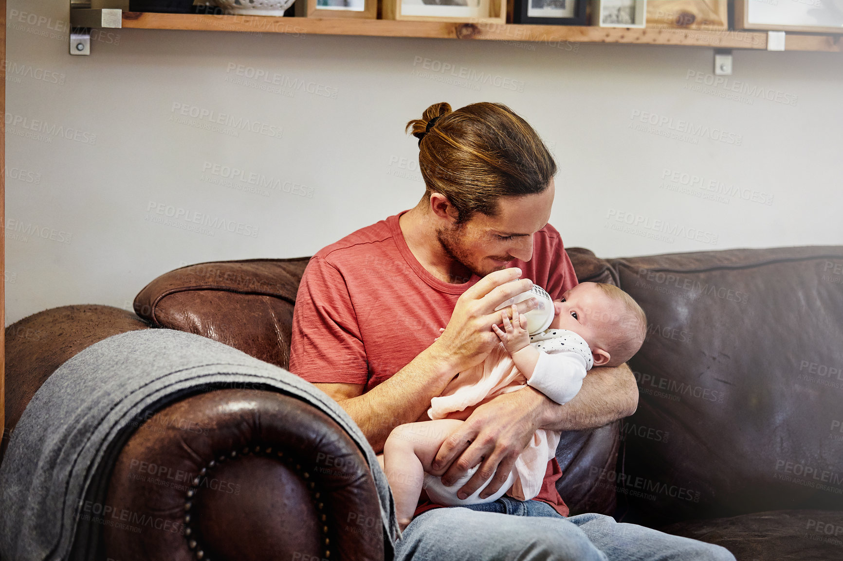 Buy stock photo Shot of a handsome young man feeding his newborn baby girl on the sofa at home