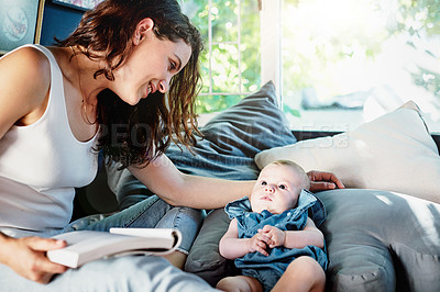 Buy stock photo Shot of an attractive young woman reading a book while keeping an eye on her newborn daughter