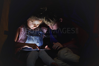 Buy stock photo Shot of a little girl and her brother using a tablet while sitting down on a bed