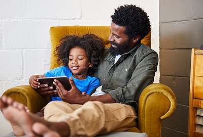 Buy stock photo Shot of a cheerful young father and son relaxing on a chair while browsing on a digital tablet at home