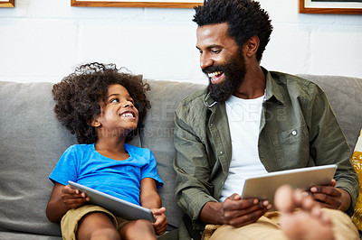 Buy stock photo Shot of a cheerful young father and son each browsing on a digital tablet while being seated on the couch at home