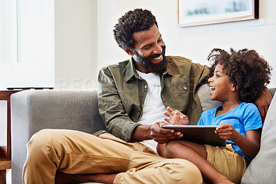 Buy stock photo Shot of a cheerful young father and son relaxing on a chair while browsing on a digital tablet at home