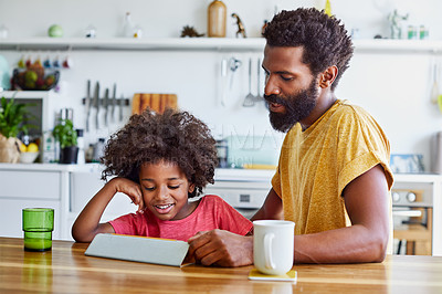 Buy stock photo Shot of a cheerful young father and son browsing on a digital tablet while having a cup of coffee in the kitchen at home