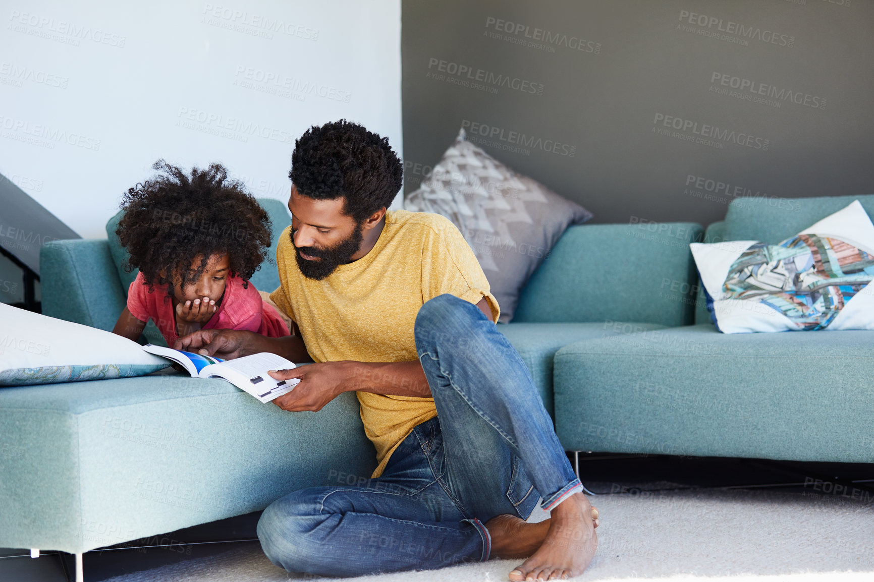 Buy stock photo Shot of a cheerful young father and son reading a storybook while being seated on a couch at home