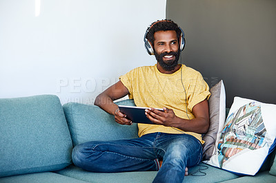 Buy stock photo Shot of a focused young man listening to music through headphones while being seated on a couch at home