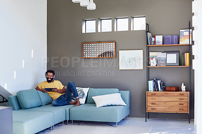 Buy stock photo Shot of a focused young man listening to music through headphones while being seated on a couch at home