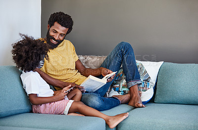Buy stock photo Shot of a cheerful father and son listening to music and reading a book while relaxing on a couch at home