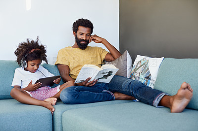 Buy stock photo Shot of a cheerful father and son listening to music and reading a book while relaxing on a couch at home