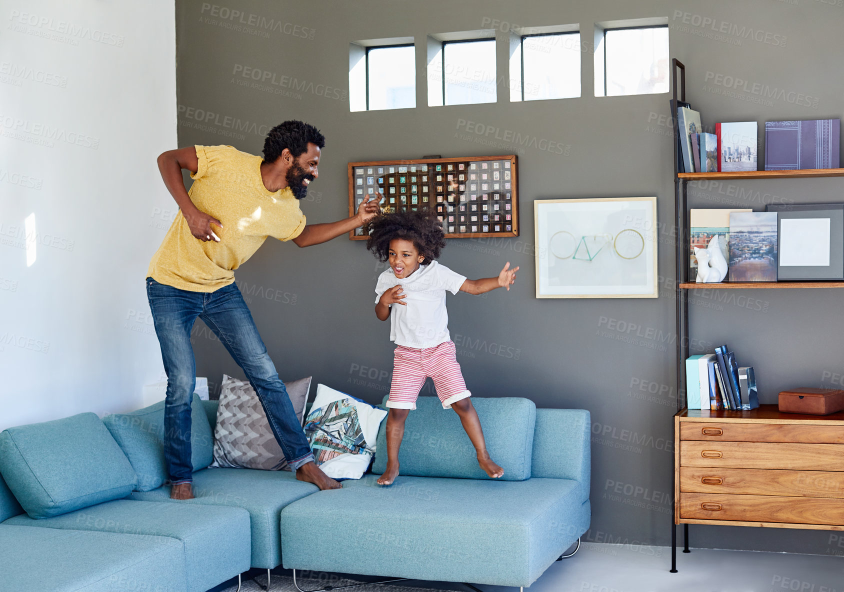 Buy stock photo Shot of a cheerful young father and his son dancing on a couch while listening to music at home during the day
