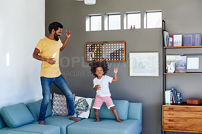 Buy stock photo Shot of a cheerful young father and his son dancing on a couch while listening to music at home during the day