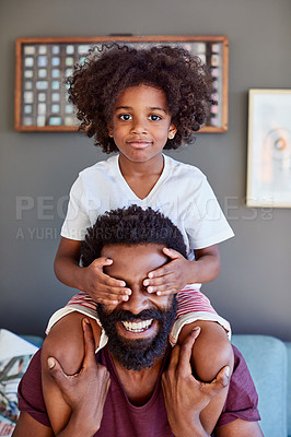Buy stock photo Portrait of a cheerful little boy sitting on his dad's shoulders while holding his dad's eyes closed inside at home during the day