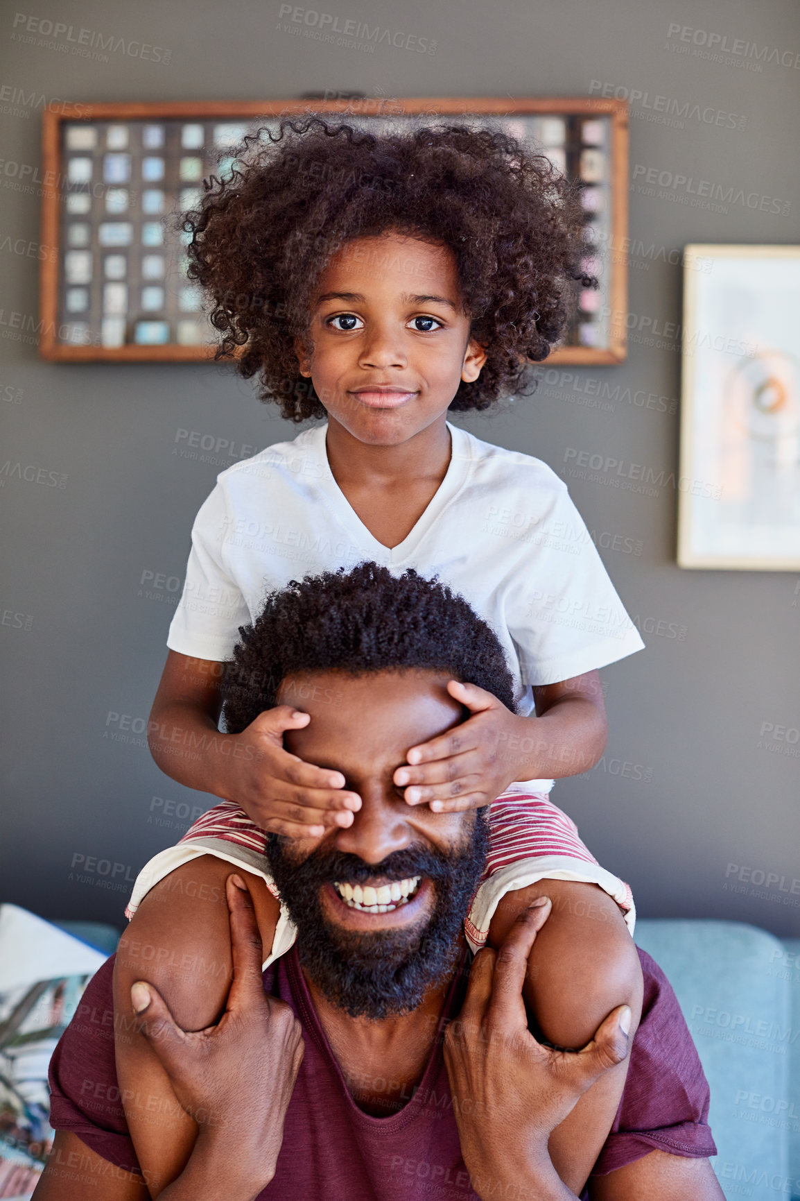 Buy stock photo Portrait of a cheerful little boy sitting on his dad's shoulders while holding his dad's eyes closed inside at home during the day