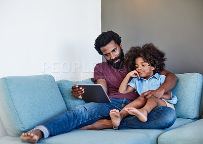 Buy stock photo Shot of a cheerful young father and son browsing on a digital tablet while relaxing on a couch at home during the day