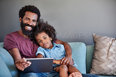 Buy stock photo Portrait of a cheerful young father and son browsing on a digital tablet while relaxing on a couch at home during the day