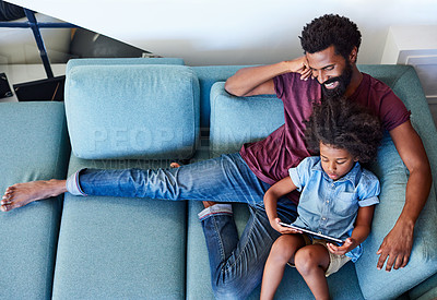 Buy stock photo High angle shot of a carefree young father and son browsing on a digital tablet while relaxing on a couch at home during the day