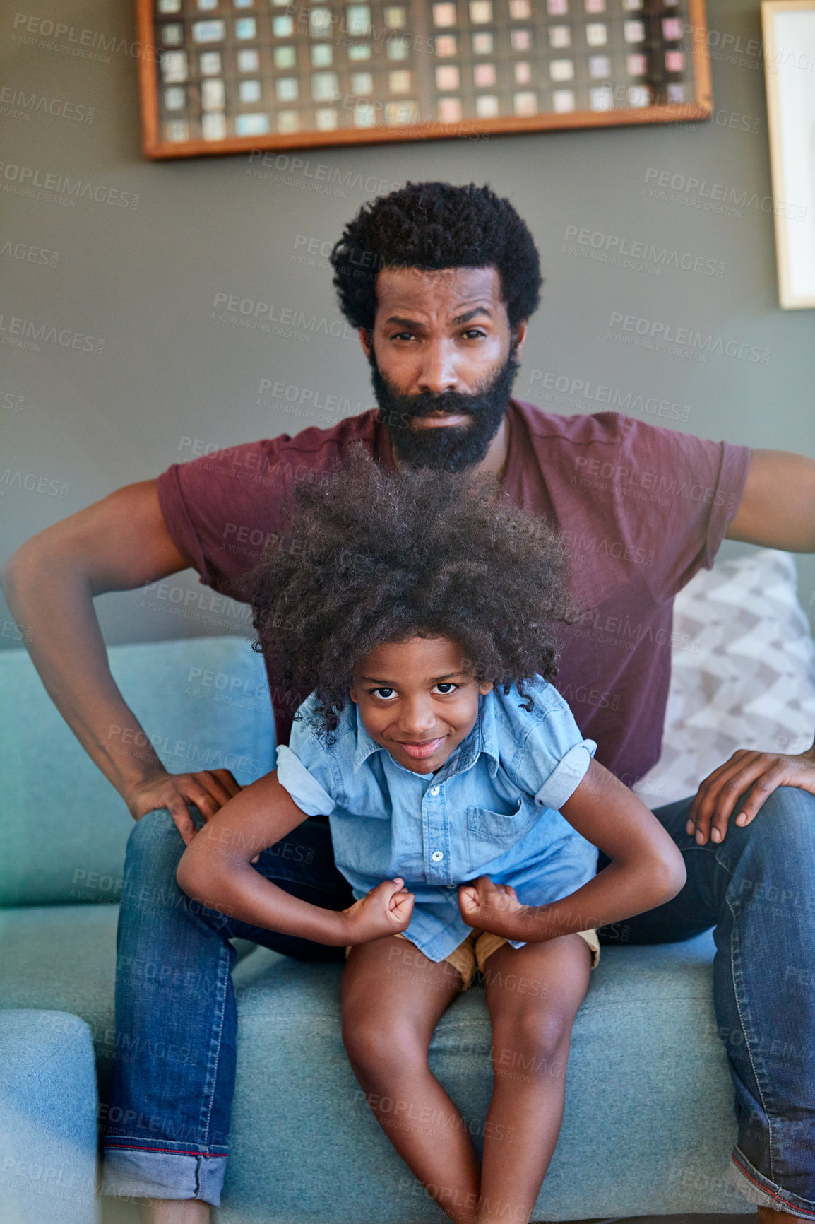 Buy stock photo Portrait of a cheerful father and son flexing their muscles while being seated on a couch at home during the day
