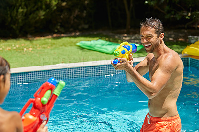 Buy stock photo Shot of a father and his son playing with water guns at the swimming pool