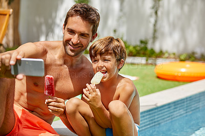 Buy stock photo Shot of a young man and his adorable son taking selfies by the swimming pool