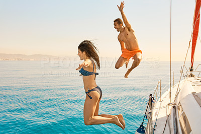 Buy stock photo Full length shot of an affectionate young couple jumping into the ocean while on a yacht cruise