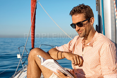 Buy stock photo Shot of a handsome young man reading a book on a relaxing boat cruise
