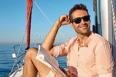 Buy stock photo Shot of a handsome young man reading a book on a relaxing boat cruise