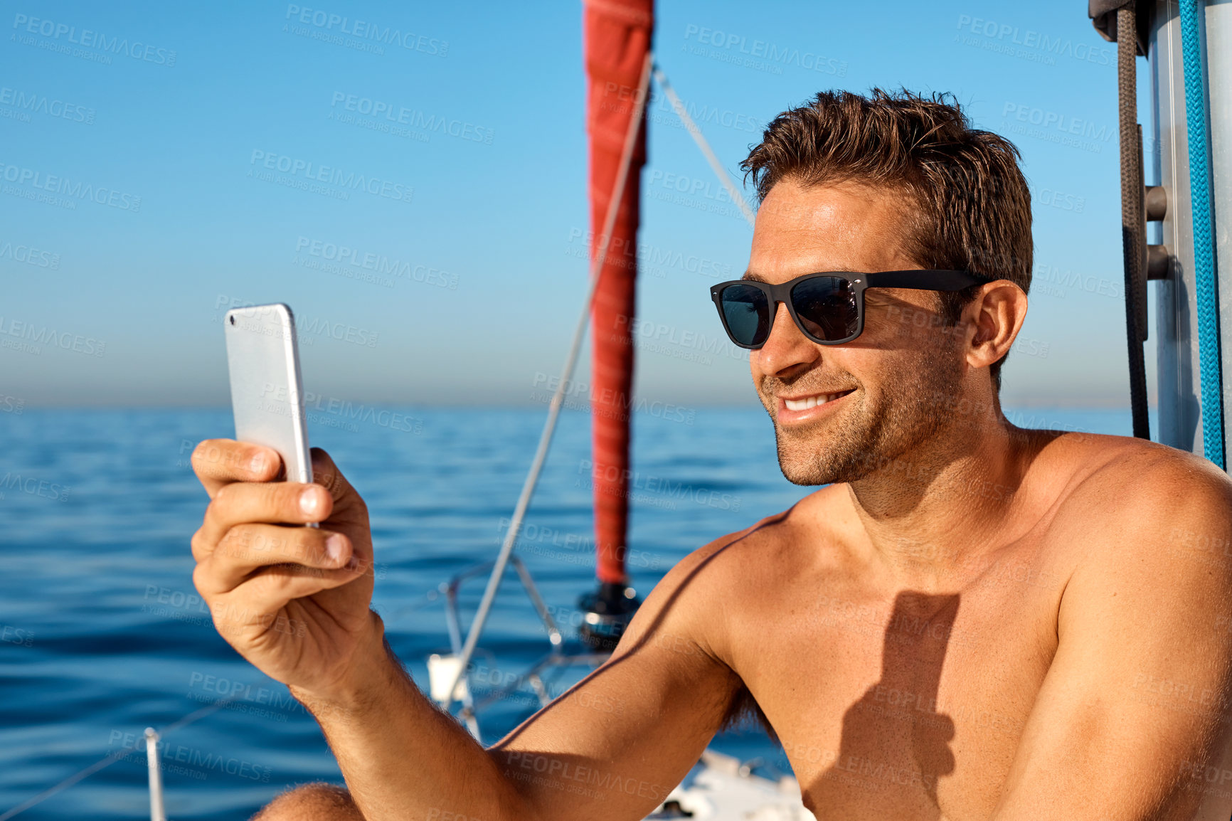 Buy stock photo Shot of a handsome young man using a mobile phone on a relaxing boat cruise